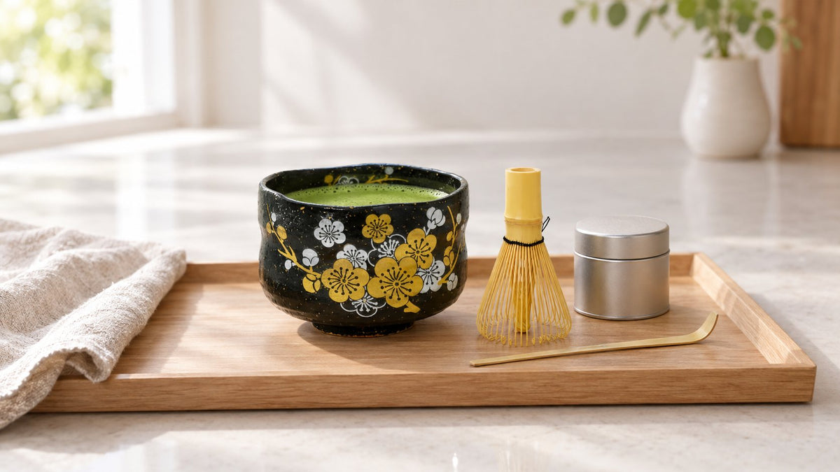 Black tenmoku plum blossom matcha bowl with whisked matcha, bamboo whisk, scoop and matcha tin on a wooden tray
